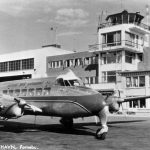 Vi ser et lite fly i forgrunnen, bildet er fra ca 1940-tallet, i bakgrunnen ser vi Fornebu flytårn med tilhørende bygninger ved siden av.